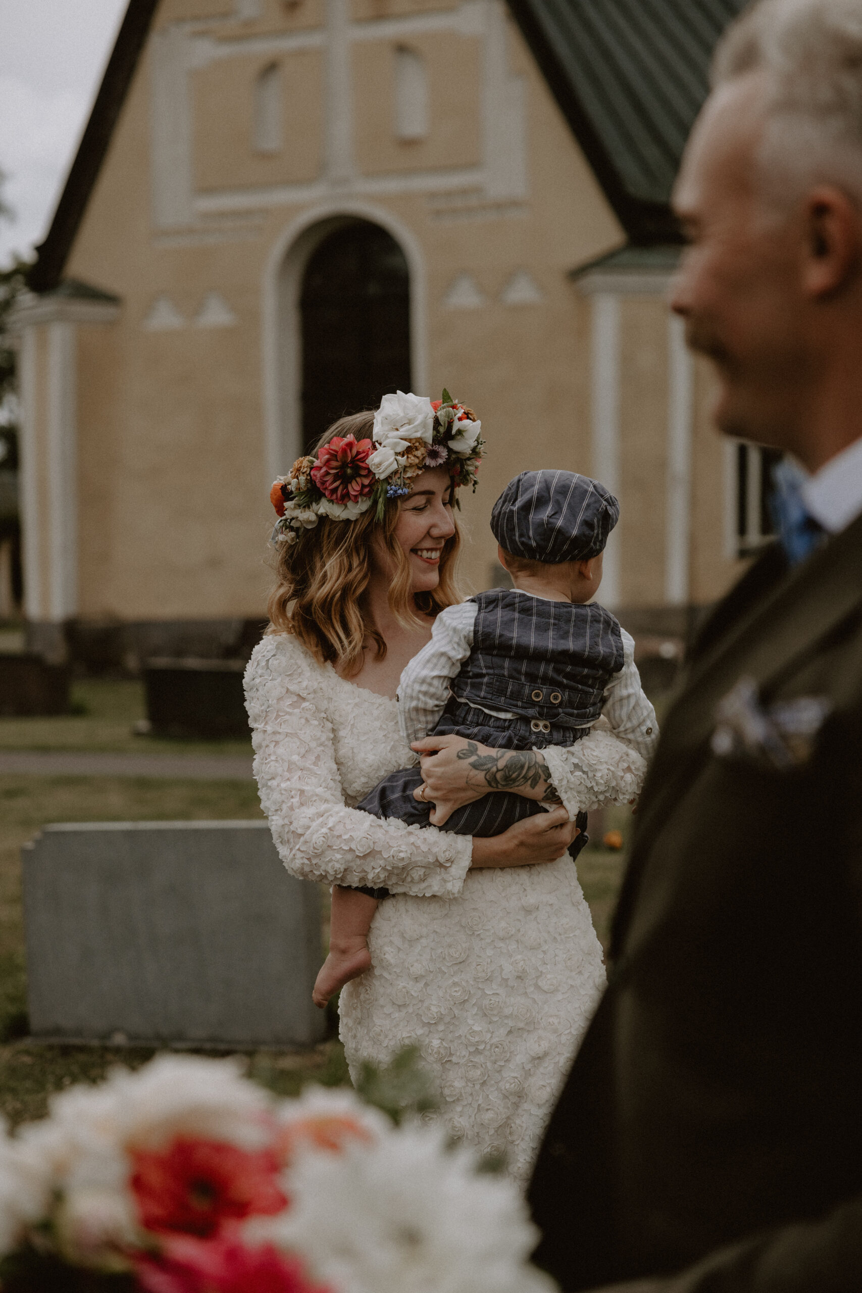 brud står framför kyrka med sin son i famnen