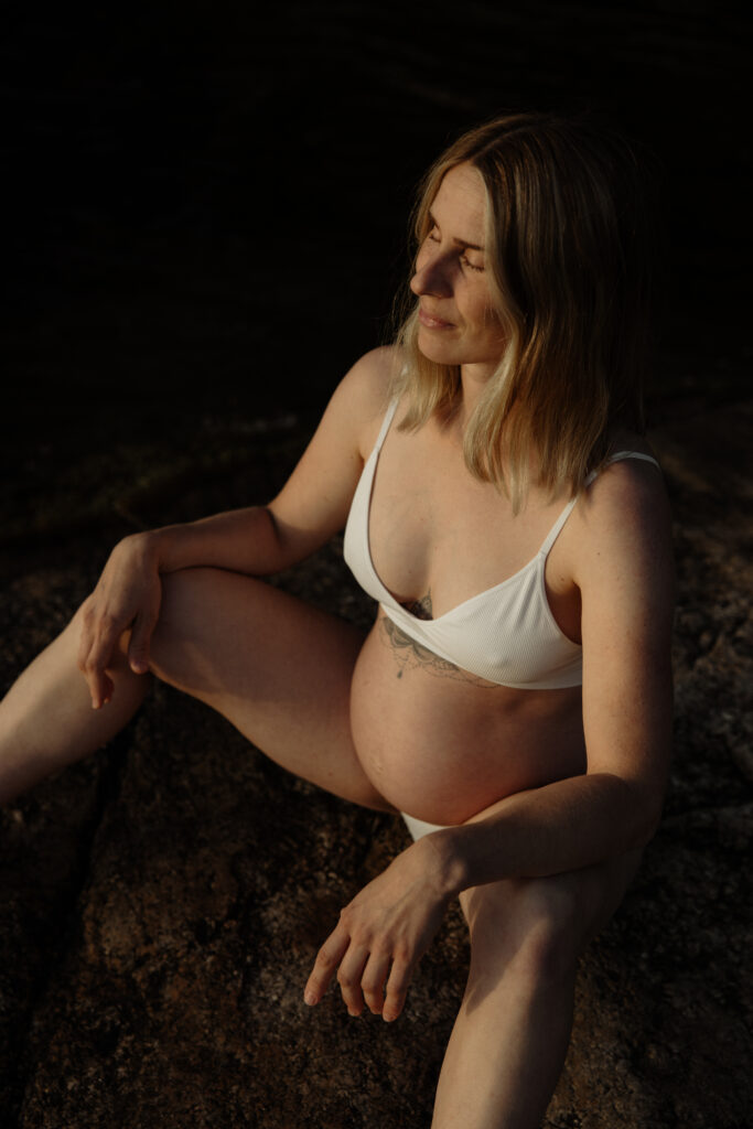 gravidfotograf västerås fotar en gravid mamma som sitter på en klippa vid vattnet och blundar ut mot vattnet