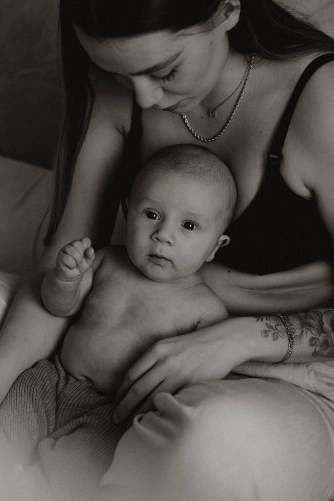 En mamma som sitter ner på sängen och har sitt barn mellan benen och kollar ner på det