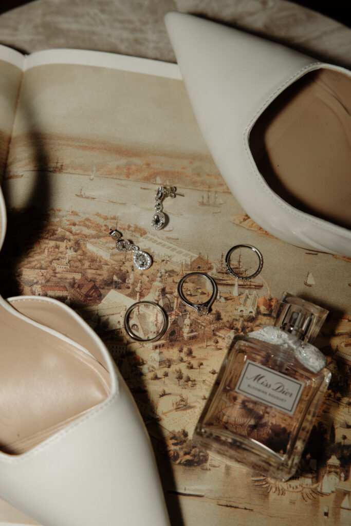 brudens skor, parfym, smycken och vigselringar liggandes på ett bord