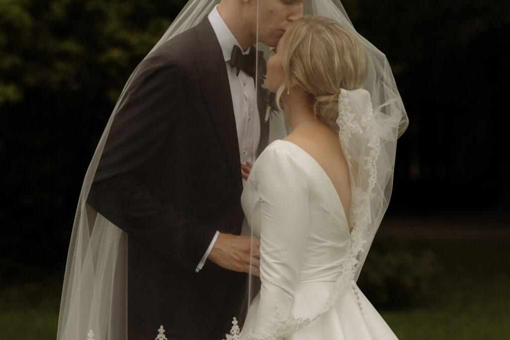 brudpar står under slöjan och kysser varadra