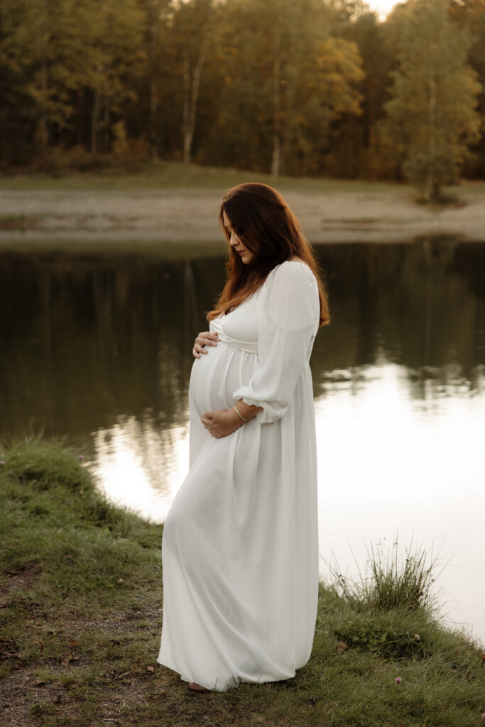 gravid tjej i mjuk klänning står vid en sjö