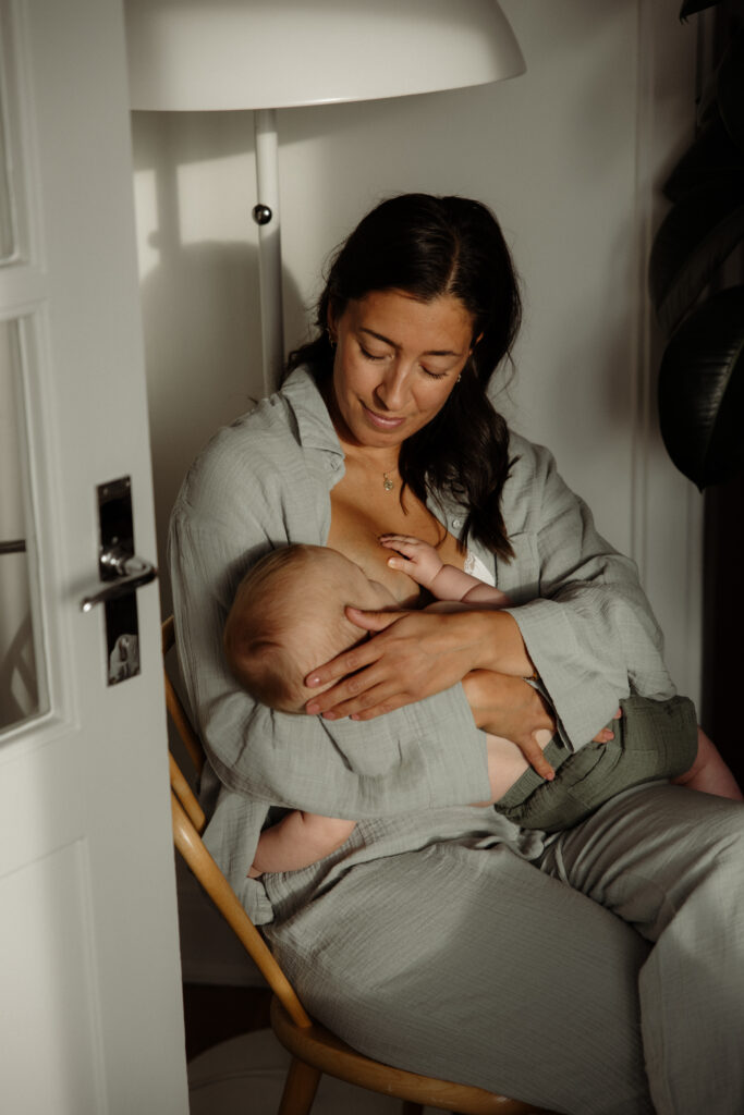 mamma sitter på en stol i vardagsrum och ammar sin bebis