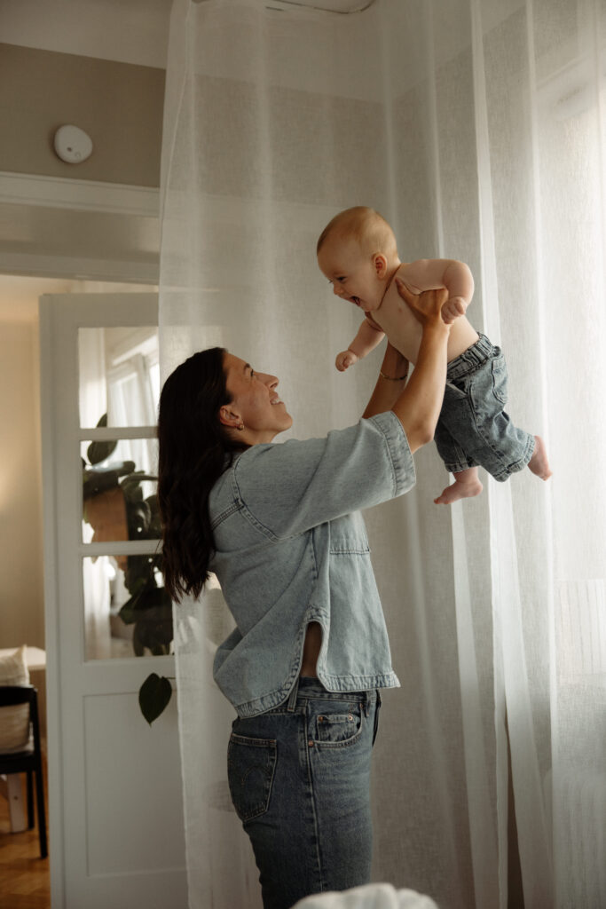 mamma håller upp sin bebis med utsträckta armar i sitt sovrum