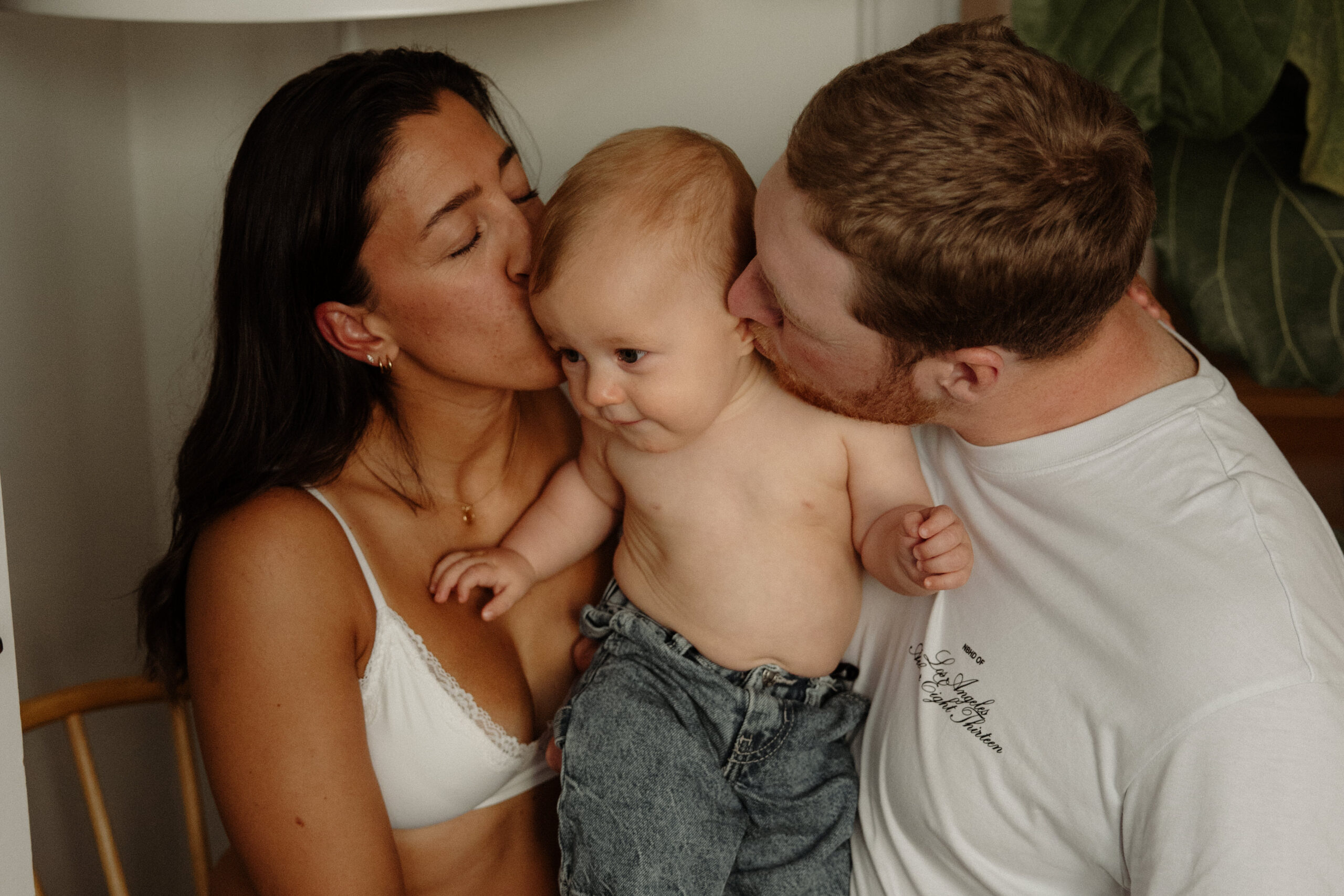 en mamma och pappa pussar sin bebis i sitt vardagsrum