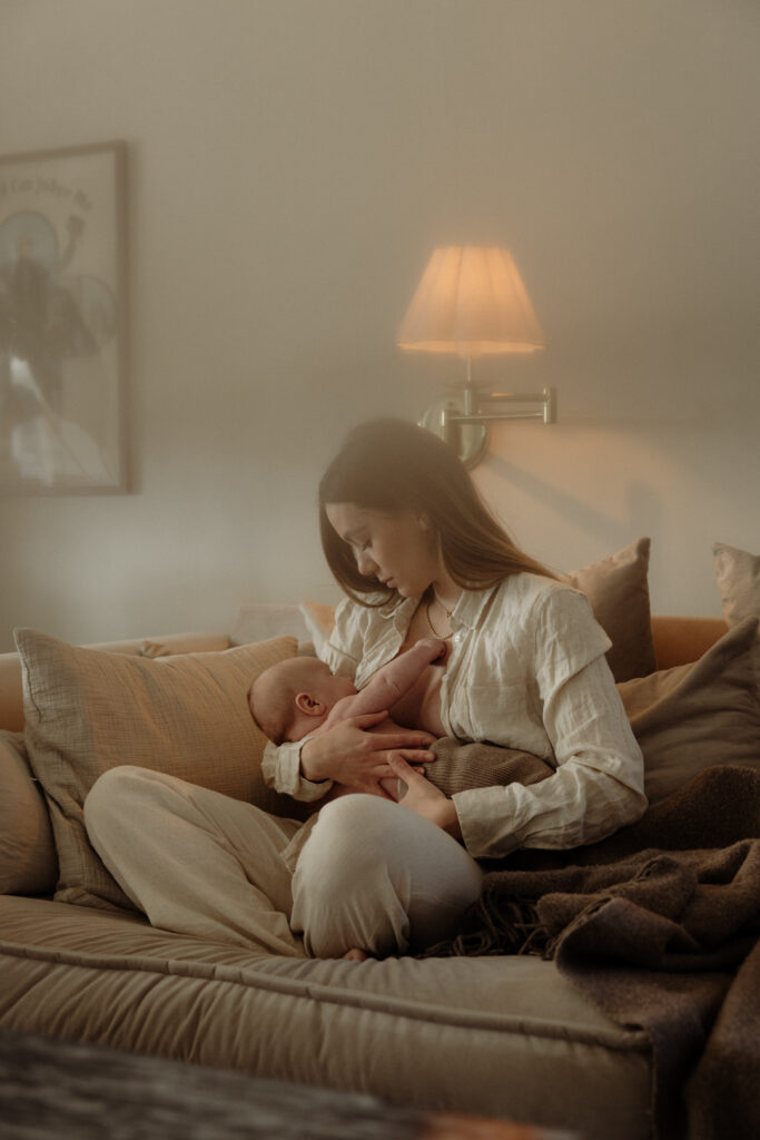 en mamma sitter i sin soffa i vardagsrummet och ammar sin bebis