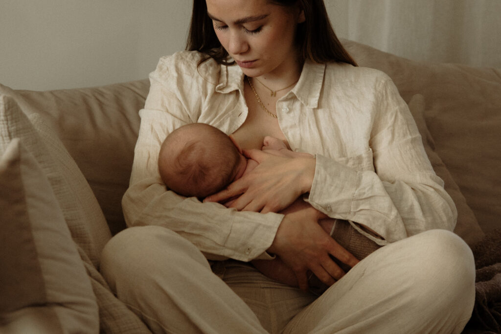 en mamma sitter i sin soffa och ammar sin bebis